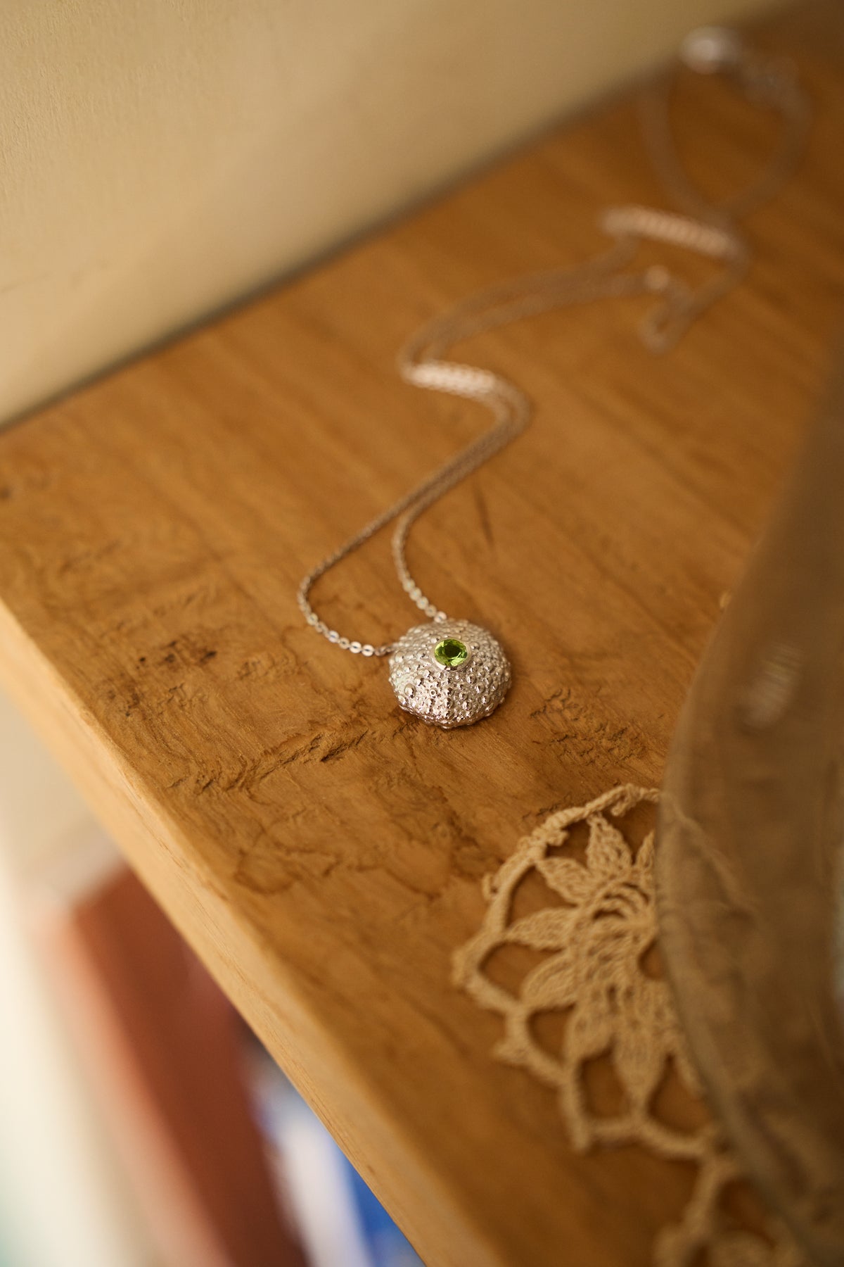Feggeri Ahinos peridot necklace in sterling silver resting beside a book on wood