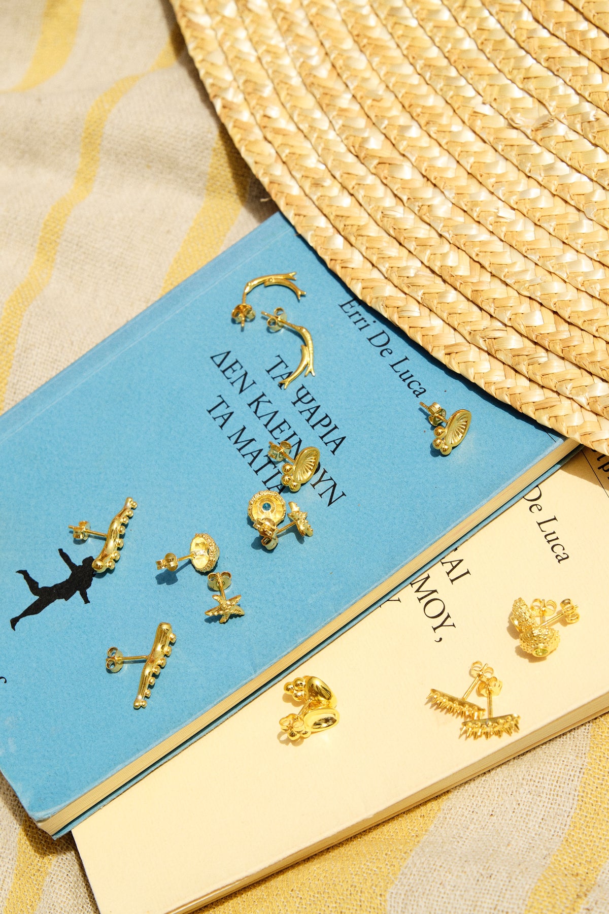 Feggeri Aegea gold vermeil stud earrings arranged on a book beside a straw hat