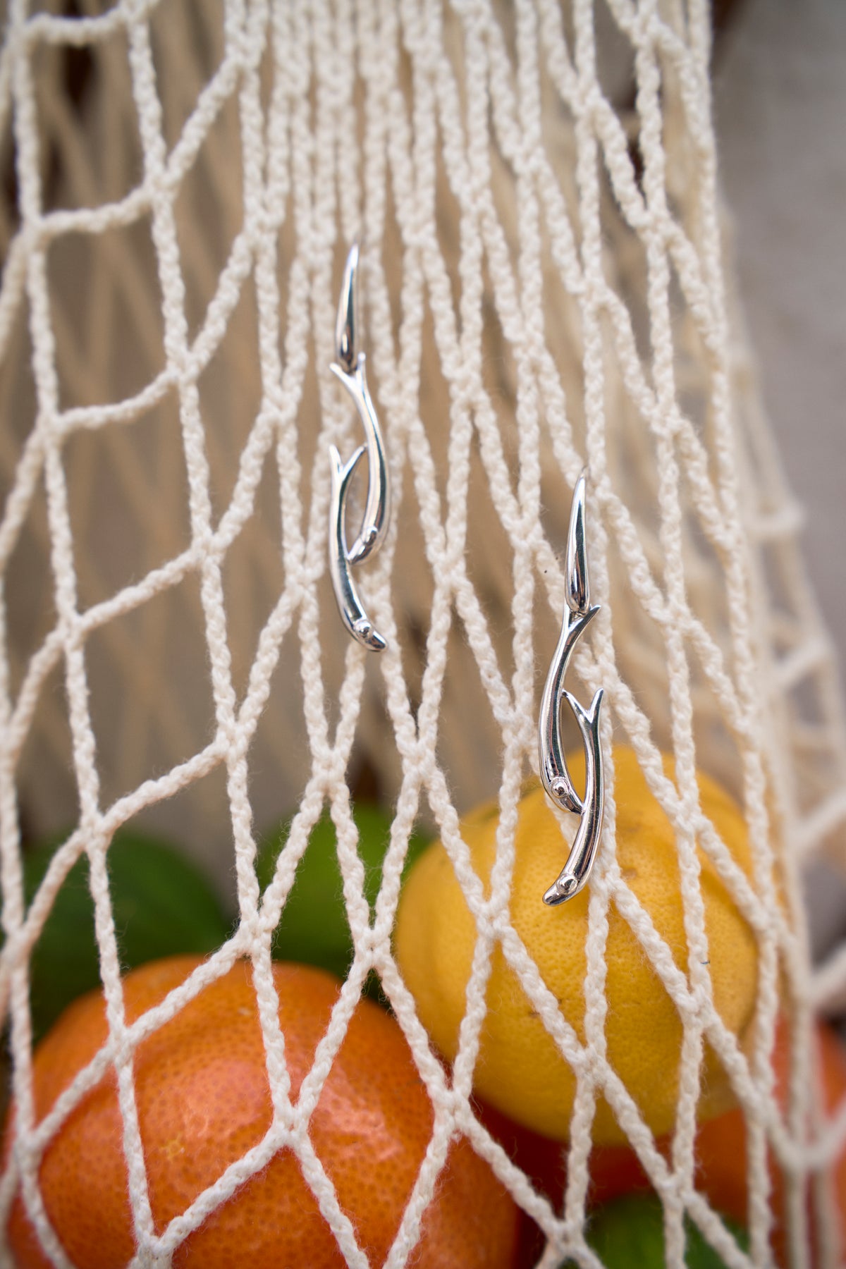 Feggeri Psari fish drop earrings in sterling silver on a net bag beside fruit