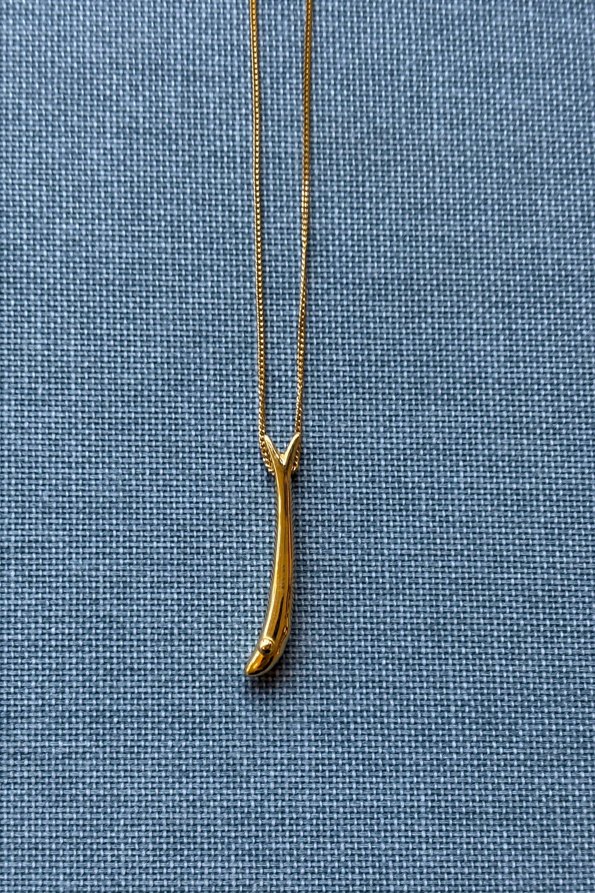 Feggeri Psari fish necklace in gold vermeil resting on denim