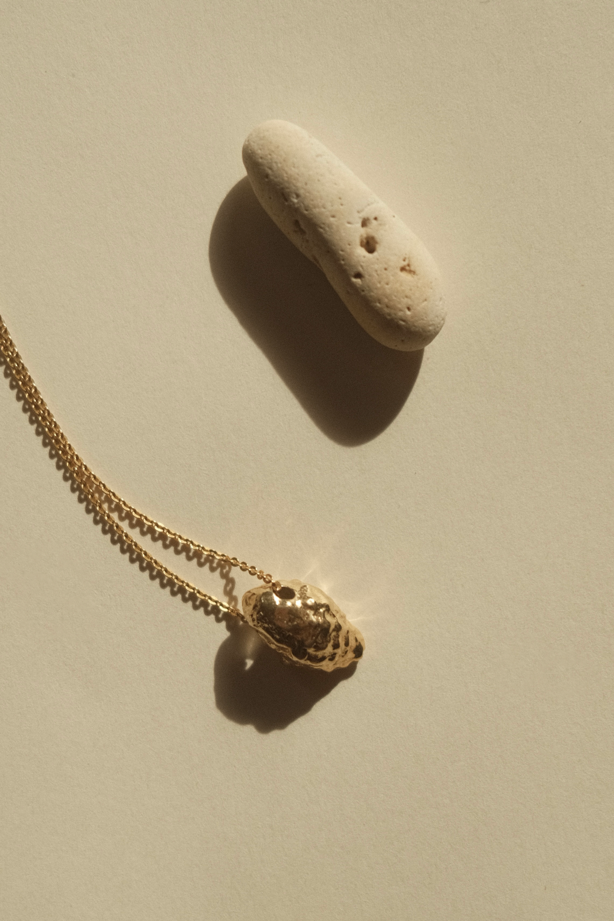 Feggeri Conch Shell necklace in gold vermeil on a ledge beside a pebble